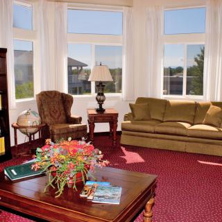 A cozy living room with large windows, featuring a sofa, armchair, and a coffee table decorated with flowers.