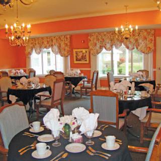 A well-decorated dining room with neatly set tables, elegant chandeliers, and large windows.