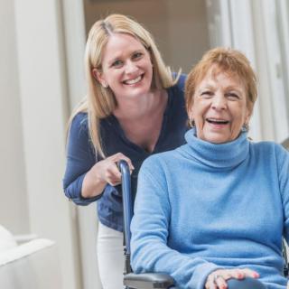 A caregiver smiling with an elderly woman in a wheelchair.