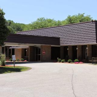 A modern single-story building with a welcoming entrance surrounded by green trees.
