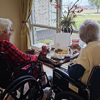 Two elderly women enjoying a snack while seated by the window.