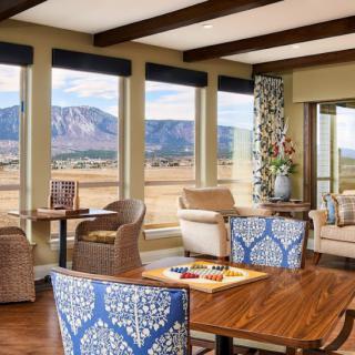 A cozy living room with large windows showcasing a beautiful mountain view, featuring comfortable seating and a stylish table.