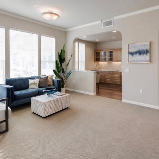 A modern living room with a blue sofa, coffee table, and large windows, leading into a kitchen.