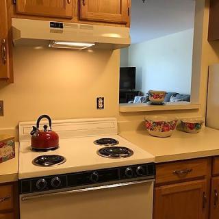 A cozy kitchen with a stove, red teapot, and wooden cabinets.