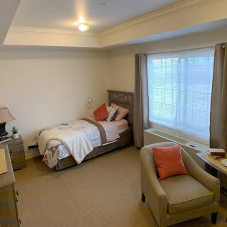A cozy bedroom with a single bed, armchair, and large window.