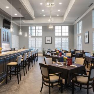 A modern restaurant interior featuring a bar area with high stools and a dining space with several tables and chairs.