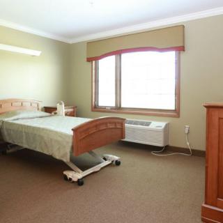 A hospital room with a bed and window, featuring simple furniture.