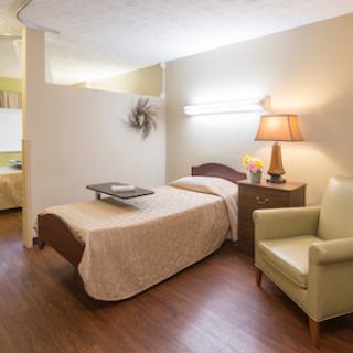 A cozy and well-lit bedroom featuring a neatly made bed, a bedside table with a lamp, and a comfortable chair.
