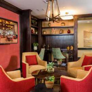 A cozy living room with vibrant red and beige chairs, a central coffee table, decorative shelving, and warm lighting.