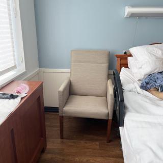 A hospital room with a beige chair beside a bed and window.