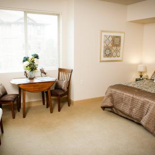 A cozy bedroom interior with a bed, small table, and chairs near a window.