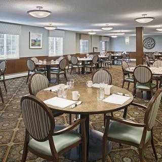 An elegantly set dining room with round tables and cushioned chairs.