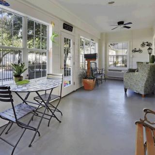 A bright sunroom with large windows, featuring a seating area and potted plants.
