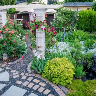 A beautifully landscaped garden featuring a stone pathway surrounded by vibrant flowers and lush greenery.