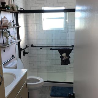A modern bathroom with glass shower doors, white tiles, and black fixtures.