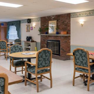 A cozy common room featuring tables and chairs arranged around a fireplace, creating a welcoming atmosphere.