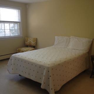 A simple bedroom with a neatly made bed near a window letting in natural light.