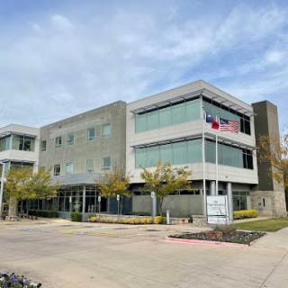 A contemporary office building with large glass windows, set against a partly cloudy sky.