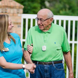A caregiver assists an elderly man outdoors, providing support and companionship.