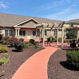 A well-maintained garden with a red pathway leading to a house, featuring a pergola along the path.