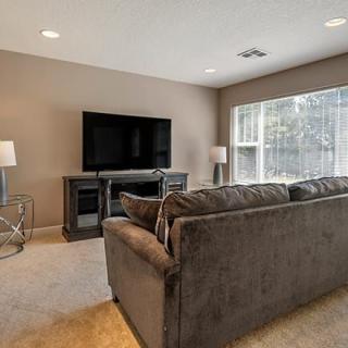A cozy living room with a comfortable sofa, large television, and ample natural light from the windows.