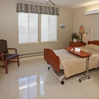 A tidy hospital room featuring a bed, chair, side table, and window with curtains.