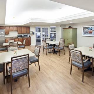 A spacious dining area with multiple tables and chairs, featuring a wooden floor and an adjoining kitchen.