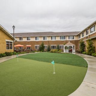 A well-maintained courtyard with a putting green and pathway, surrounded by a two-story building.