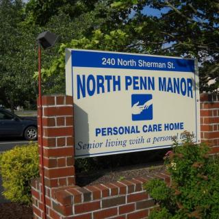Sign for North Penn Manor Personal Care Home on a brick wall surrounded by greenery.