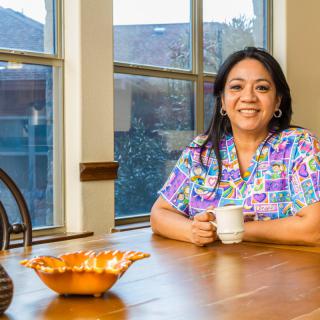 A woman smiling while sitting at a kitchen table with a coffee cup.