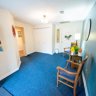 A cozy waiting room with blue carpet and wooden chairs.