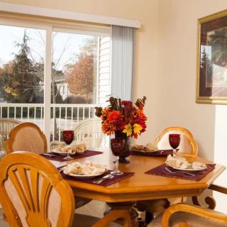 A cozy dining area with a wooden table set for a meal, featuring a floral centerpiece and natural light streaming through the window.