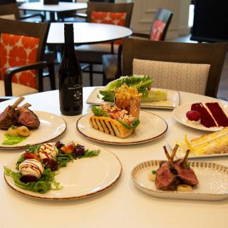 A gourmet dining setup featuring lamb chops, desserts, and a bottle of wine on a restaurant table.