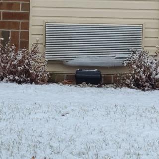 A snowy landscape featuring an outdoor air conditioning unit next to a building.