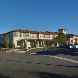 A large, two-story building with a parking lot in front, set against a clear blue sky.