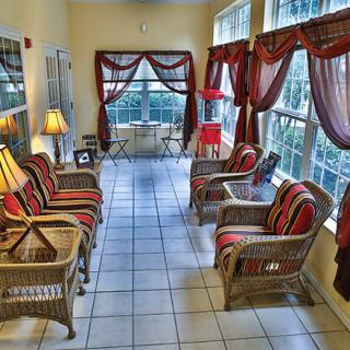 A cozy sunroom featuring wicker furniture, large windows with curtains, and ambient lighting.