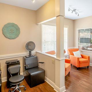 A modern salon with a hair drying station and a cozy waiting area featuring bright orange chairs.