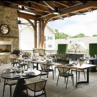 An elegantly set outdoor dining area with neatly arranged tables and chairs under a wooden roof, offering a cozy ambiance.
