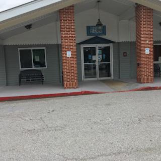 A welcoming entrance of a brick building, featuring large glass doors and a sloped roof.