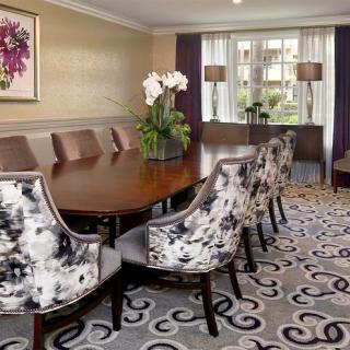 A well-designed dining room featuring a long table with upholstered chairs, a decorative carpet, and elegant floral arrangements.
