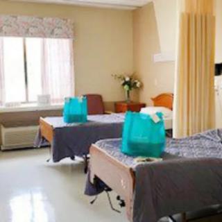 A hospital room with two beds separated by a curtain and a window in the background.