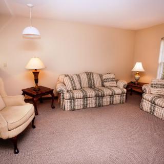 A cozy living room featuring plaid sofas and armchairs, complemented by warm lighting and carpeted flooring.