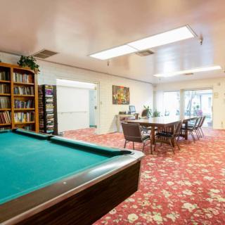A cozy recreation room featuring a pool table, bookshelves, and a large dining table with floral carpeting.