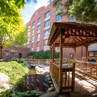 A hotel building with a landscaped garden featuring a wooden gazebo and pond.