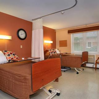 A shared hospital room with two patient beds, featuring warm colored walls and a large window.