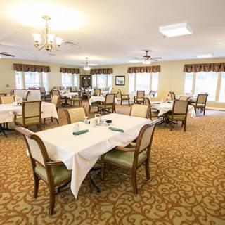 A spacious dining room with several tables and chairs, elegant decor, and well-lit chandeliers.