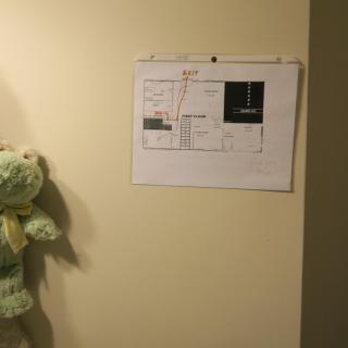 A teddy bear hangs on a wall next to a paper with a floor plan.