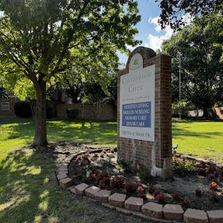 A welcoming sign set in a lush green landscape with trees and well-maintained flower beds.