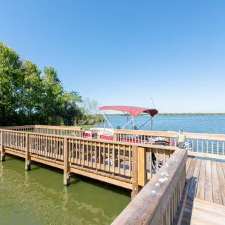 A wooden dock with a boat on a tranquil lake surrounded by trees under a clear blue sky.