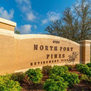 Entrance sign for North Port Pines Retirement Villas surrounded by lush greenery.